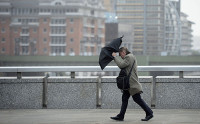 A commuter loses control of his umbrella as he braves the wind and rain while crossing London Bridge in London